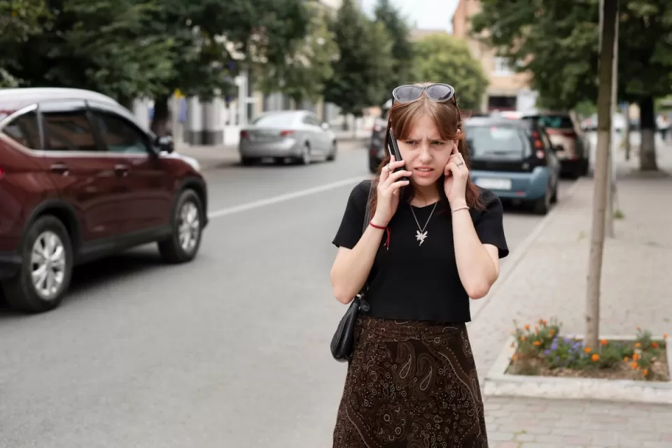 Girl on phone struggling to hear standing on loud city street.